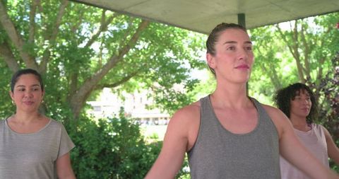 Women stretching together under concrete shelter near leafy trees during outdoor workout