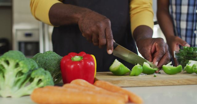 Man chopping fresh vegetables including broccoli, bell peppers, and carrots on a cutting board in a kitchen. Ideal for content about healthy eating, meal preparation, cooking tutorials, and promoting a balanced diet. Can be used in blogs, educational materials, and promotional campaigns centered on culinary skills and nutrition.