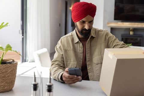 Indian man in red turban at home handling box and checking phone