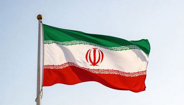 Iran flag waving over clear sky with emblem and tricolor green white red stripes