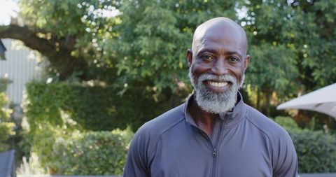 Mature african man smiling in sunlit backyard wearing zip-up athletic jacket, portrait