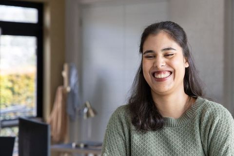 Young woman smiling and leaning forward in cozy home office wearing green sweater