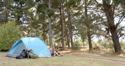 Two Women Relaxing at Wooded Campsite with Blue Tent