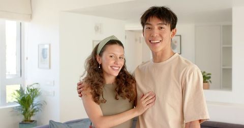 Smiling young couple embracing in bright modern living room with neutral tones and plants