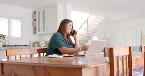 Businesswoman on Phone using Laptop in Bright Home Office