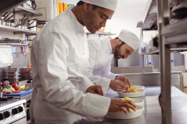 Two chefs garnishing food in commercial kitchen at restaurant