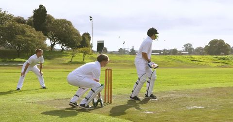 Male cricketer batting with wicketkeeper on field in daylight