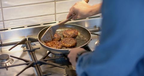 Mid adult male flipping beef burger patties in nonstick pan on gas stove, home cooking