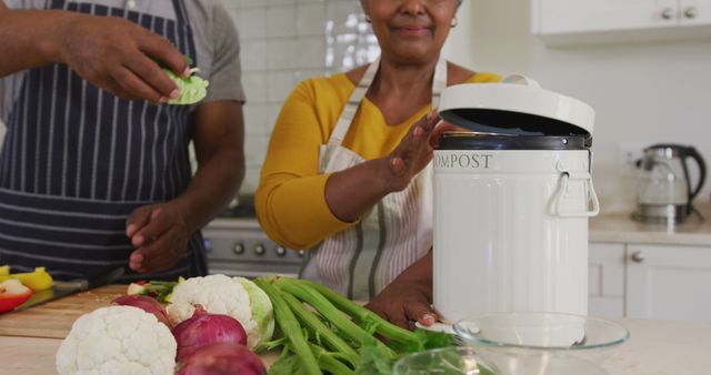A couple recycling food scraps into a compost bin in a bright, modern kitchen with cut vegetables on the counter. This image can be used for promoting eco-friendly lifestyle, zero waste initiatives, sustainable living, and health-conscious cooking practices.