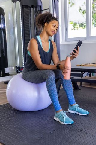 Fit Woman Balancing on Exercise Ball with Smartphone in Gym