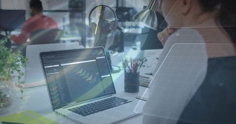 Focused programmer analyzing code dashboard on laptop in modern open-plan office