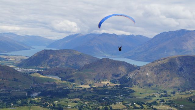 Paraglider flying high above a breathtaking mountainous terrain with scenic lake views. Suitable for promoting tourism, outdoor and adventure activities, travel agencies, or nature conservation. Perfect for visual content related to freedom, sports, and travel experiences.