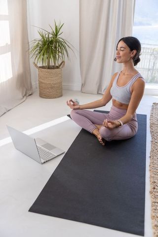 Woman practicing guided yoga and meditation at home with laptop headset, natural light