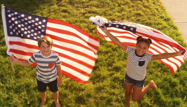 Kids waving american flags on sunny lawn jumping and smiling for fourth of july fun