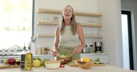 Elderly Woman Joyfully Preparing Healthy Salad in Modern Kitchen