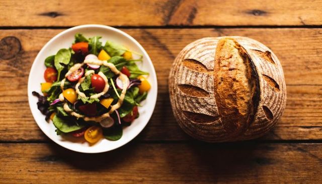 Rustic sourdough loaf resting beside fresh garden salad overhead on wooden table