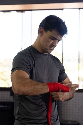 Mid-adult man wrapping red handwraps for boxing training, focused preparation