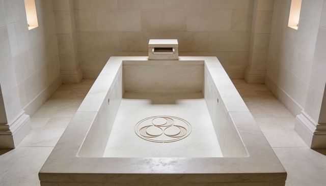 Minimalist limestone spa basin in symmetrical stone chamber with carved circular medallion