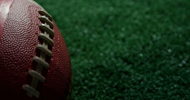 Close-up of an American football on a textured green turf, with copy space. The focus on the laces and the texture of the ball suggests the intensity and details of the sport.
