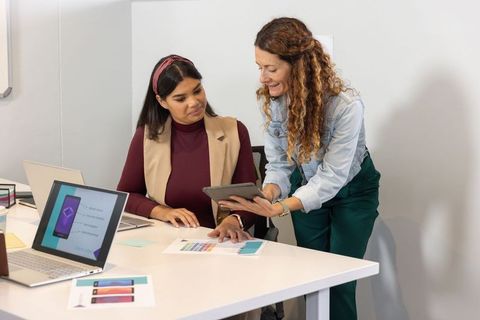 Female coworkers collaborating over phone mockups and color palette at office table