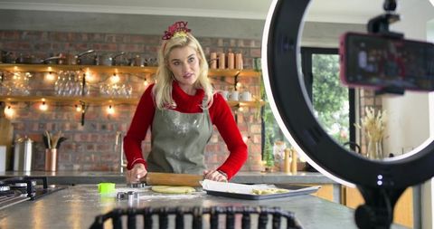 Baking vlogger rolling dough on rustic brick kitchen island while filming with ring light