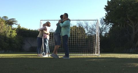 Family embracing on backyard turf with soccer goal: bonding and recreation