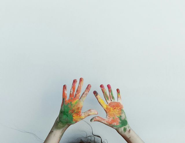 Two hands covered in colorful paint shown against a plain white background, symbolizing artistic creativity and expression. This can be used in art-related blogs, educational content on creativity for children, or promotional material for art classes and creative events.