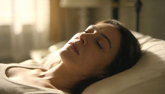 Woman reclining on bed resting with eyes closed in warm morning light, serene calm
