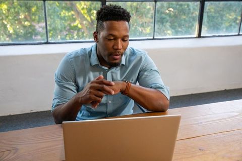 Businessman sitting with laptop checking time in modern office
