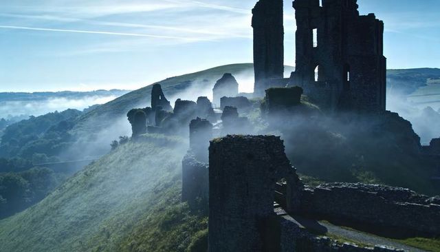 Misty medieval castle ruins standing on hilltop overlooking fog-filled valley at dawn