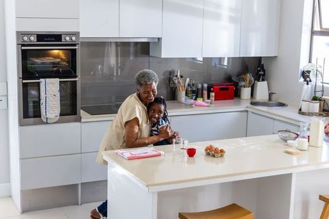African grandmother hugging granddaughter at kitchen island while baking together