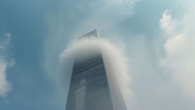 Skyscraper Piercing Through Circular Cloud Against Blue Sky