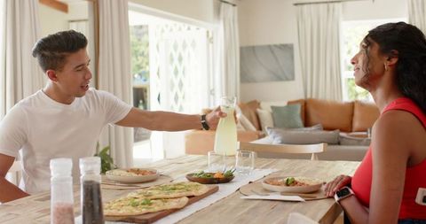 African couple sharing homemade meal while pouring lemonade at bright modern dining table