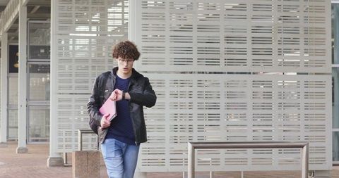 Commuter checking smartwatch while walking with pink folio at modern urban plaza