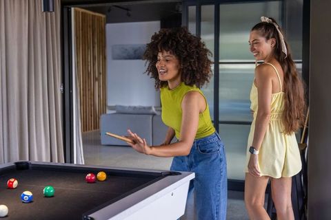 Diverse female friends playing billiards in modern home lounge, game night social fun