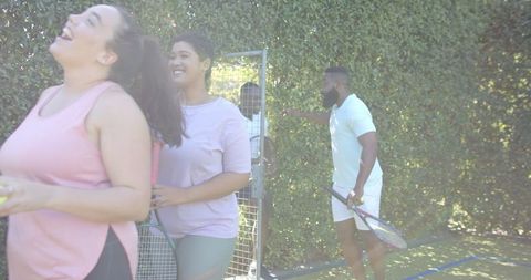 Smiling friends entering tennis court with rackets enjoying outdoor activity
