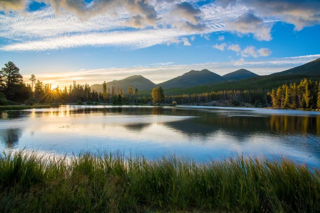 Majestic mountain scene featuring a tranquil lake reflecting the surrounding trees and clouds during a picturesque sunset. Ideal for nature backgrounds, travel advertisements, serene landscape posters, and relaxation-themed decor.