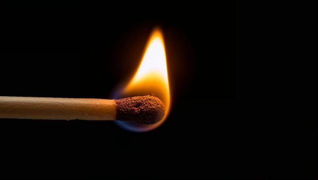 Burning matchstick close-up emitting blue-base flame and charred tip on black backdrop