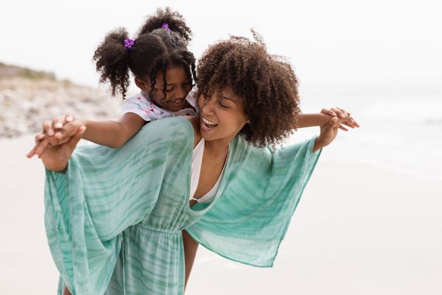 Front view of happy Biracial mother giving piggyback ride to her cute young Biracial daughter on the beach.