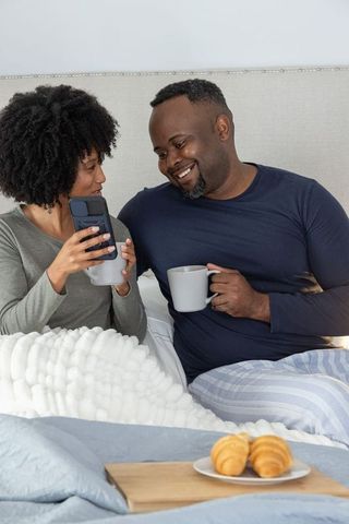 African american couple enjoying morning coffee and browsing smartphone in bed