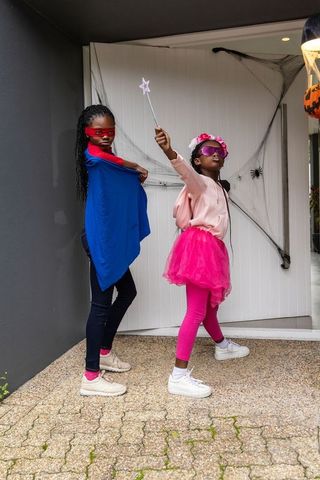 African american girls dressing as superhero and fairy celebrating halloween on porch