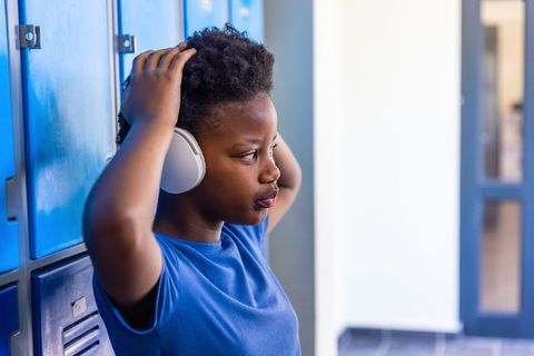 Teen african american student adjusting wireless headphones while leaning on school lockers