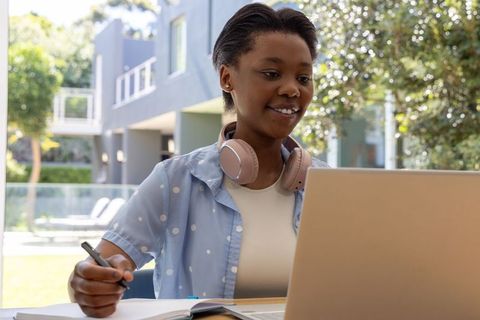 Young african woman studying on terrace with laptop and pink headphones