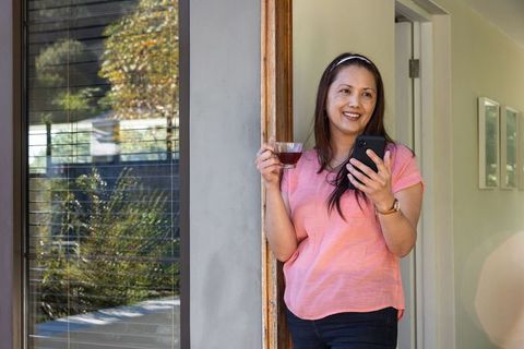 Asian Woman Leaning at Door Enjoying Coffee and Smartphone