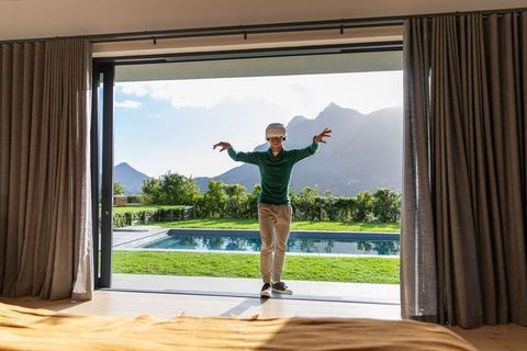 Asian man standing at sliding glass door wearing vr headset with pool and mountain view