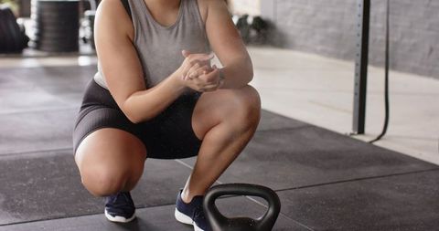 Female athlete squatting near kettlebell on gym floor preparing for strength training