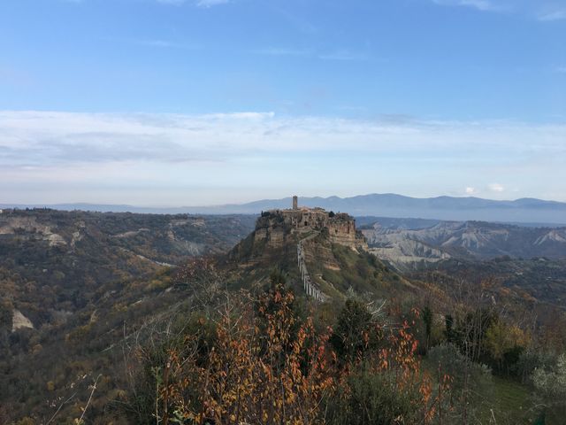 A picturesque view of Civita di Bagnoregio, an ancient hilltop town in Italy, surrounded by lush landscape and autumn foliage. Ideal for travel blogs, destination guides, tourism brochures, and cultural heritage articles.