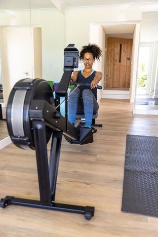 Young adult woman rowing at home gym with determination