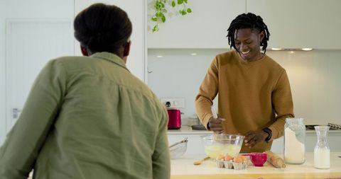 African american couple cooking breakfast in bright modern kitchen, smiling and whisking