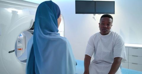 Patient sitting on ct table facing clinician wearing blue hijab, radiology consultation